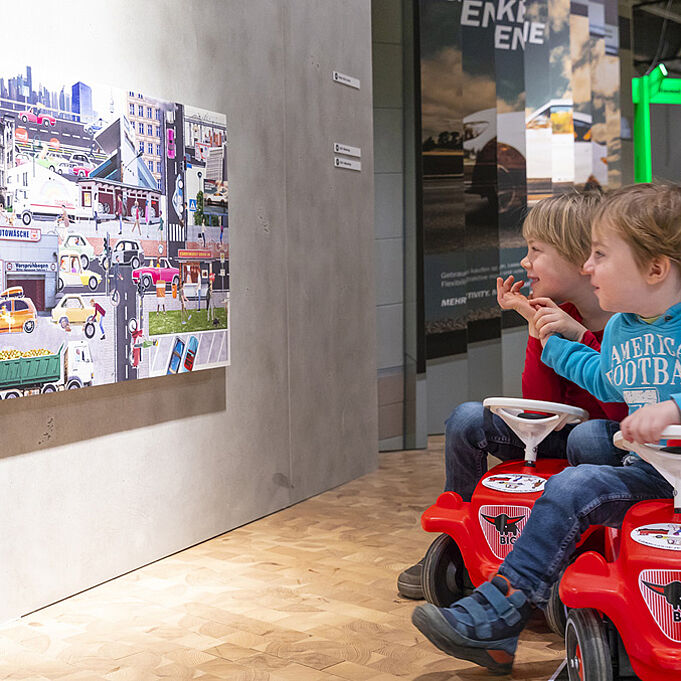 Colorful picture collage in the style of the corporate design of the exhibition hangs on the wall and is examined by two children