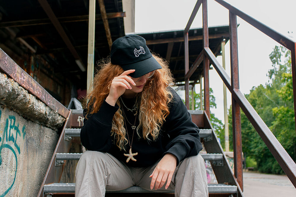 Frau mit schwarzem Basecap sitzt auf Treppe eines alten Fabrikgeländes