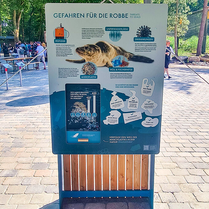 Lernstation zu "Gefahren für die Robbe". Eine Robbe ist in der Mitte der Tafel zu erkennen. Unten sind Umrisse von Plastikmüll zu erkennen. Daneben ist eine Übersicht davon, wie viele Jahre welcher Müll braucht, um abgebaut zu werden.