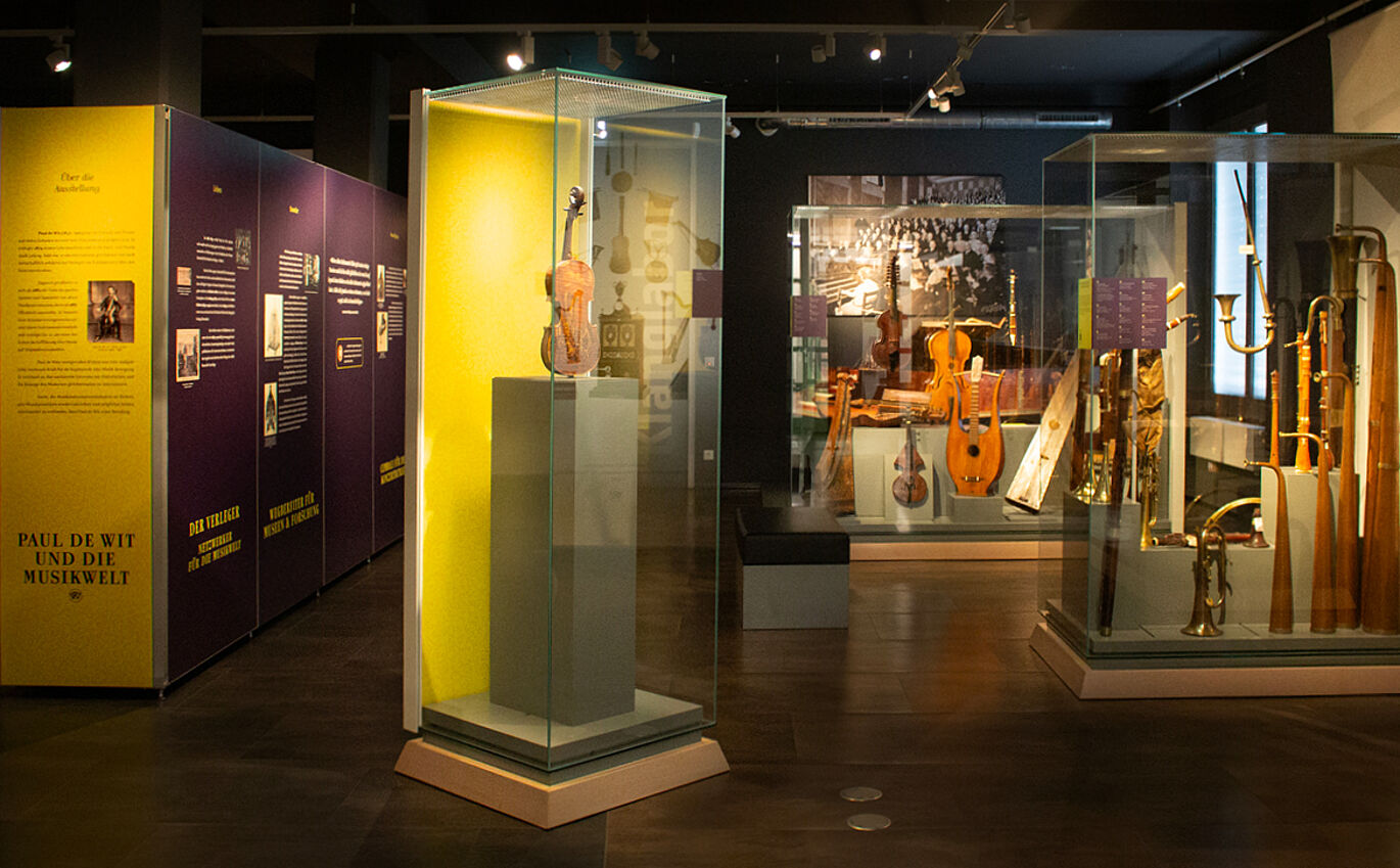 Blick in die Ausstellung: Mehrere Schaukästen mit Musikinstrumenten stehen im Raum verteilt. Links steht eine große Informationswand.