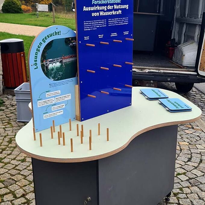 Realbild der Lernstation: Ein runder Tisch mit wellenförmigen Rändern. Auf dem Tisch ist eine dunkelblaue und eine hellblaue Informationstafel zu erkennen.