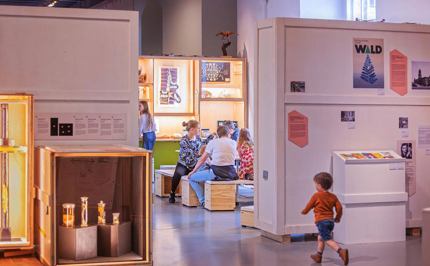 Foto Kinder und Erwachsene in einem modernen Museum mit Ausstellungsstücken in beleuchteten Vitrinen und Informationswänden