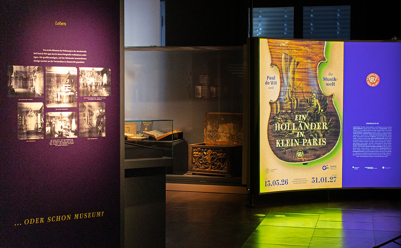 Eingangsbereich der Sonderausstellung. Rechts ist ein großes beleuchtetes Plakat mit dem Key Visual und dem Ausstellungsnamen "Paul de Wit und die Musikwelt - Ein Holländer in Klein-Paris". Links ist eine lilane Tafel zu sehen mit Fotografien in schwarz-weiß.