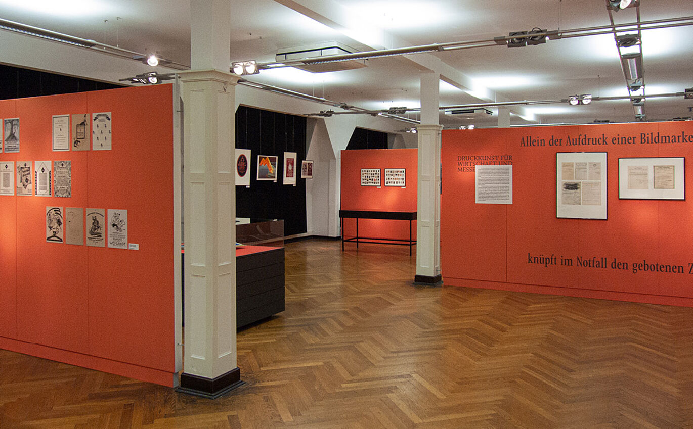 Exponate an oranger Wand als Teil der Ausstellungsgestaltung im Museum für Druckkunst