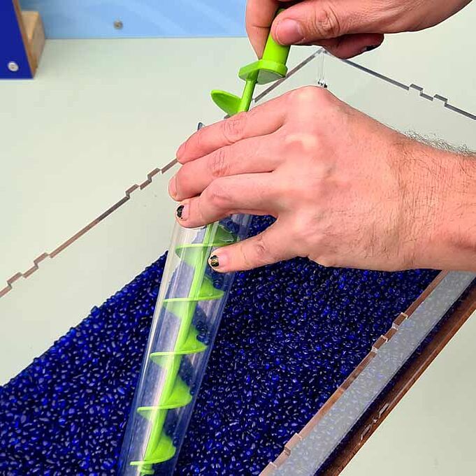 Eine Person hält die archemische Schraube in der Hand und hält sie in das blaue Granulat.