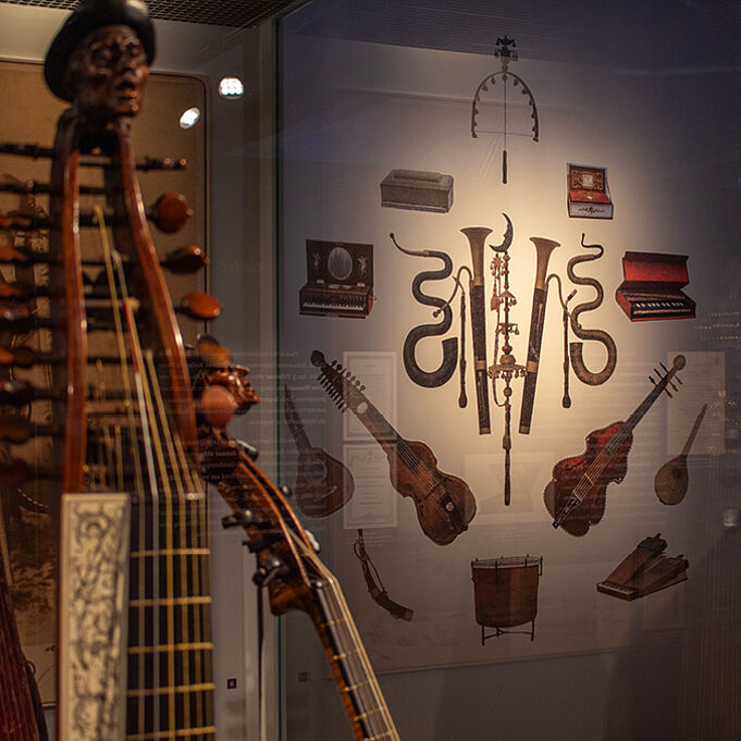 Im Vordergrund ist leicht verschwommen ein Musikinstrument zu sehen. Im Hintergrund ist ein Plakat zu erkennen, auf dem mehrere Musikinstrumente illustriert sind.