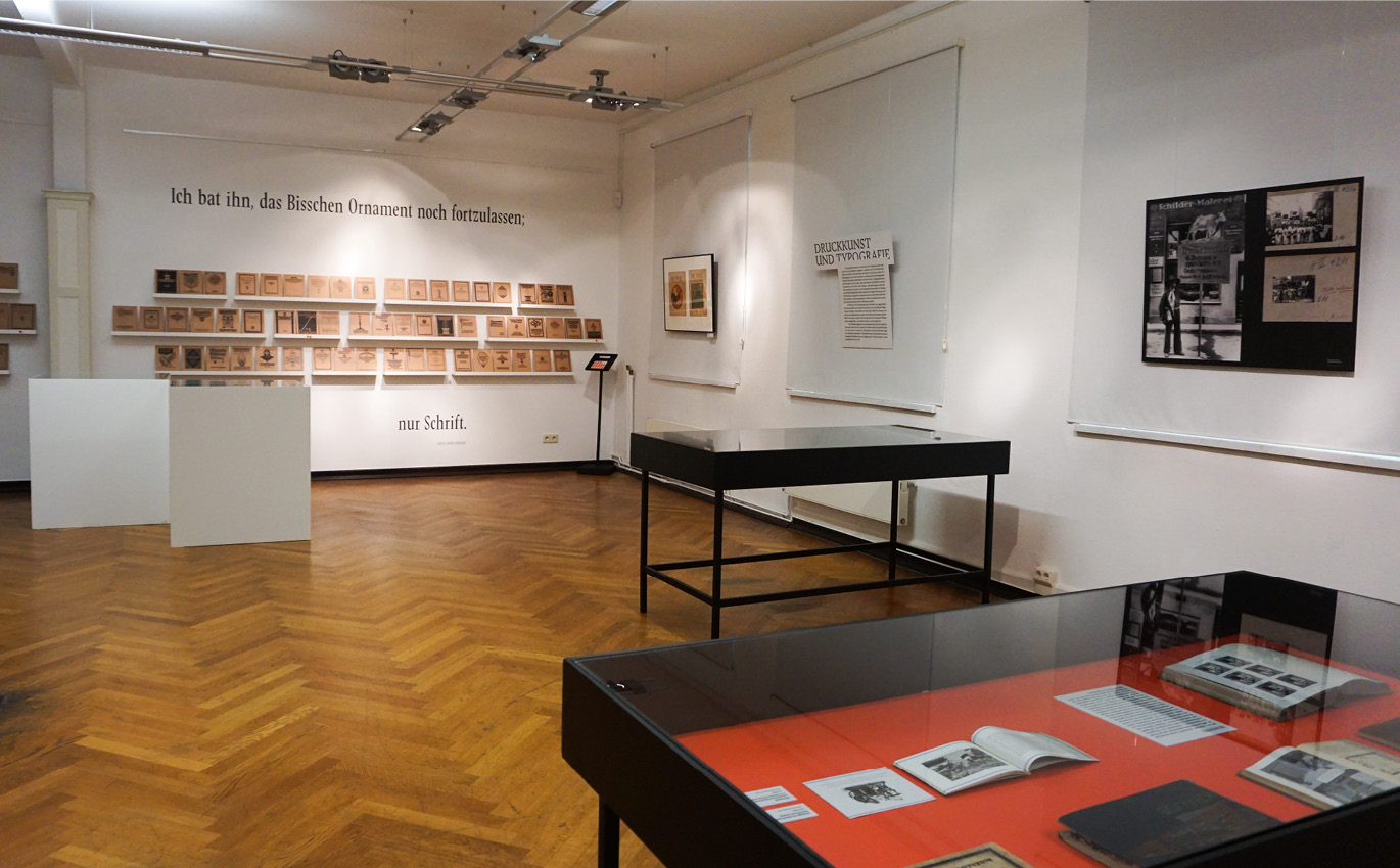 Exhibition situation: exhibits and text on a white wall and black display cabinets in the room