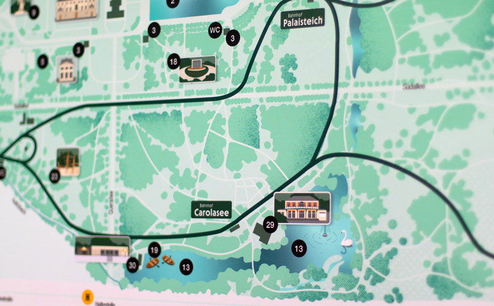 Nahaufnahme einer Informationstafel, die die Parkanlage abbildet. Zu erkennen ist der Ausschnitt um Carolasee. Schwarze Linien zeigen die Fahrroute der Parkeisenbahnen.
