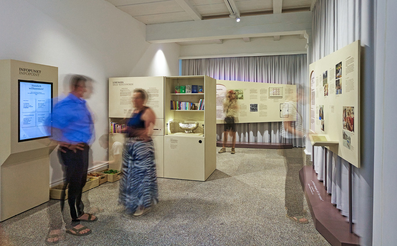 Bild der Ausstellung. Links ist ein Infopunkt. Mehrere Schemen von Menschen sind zu erkennen.