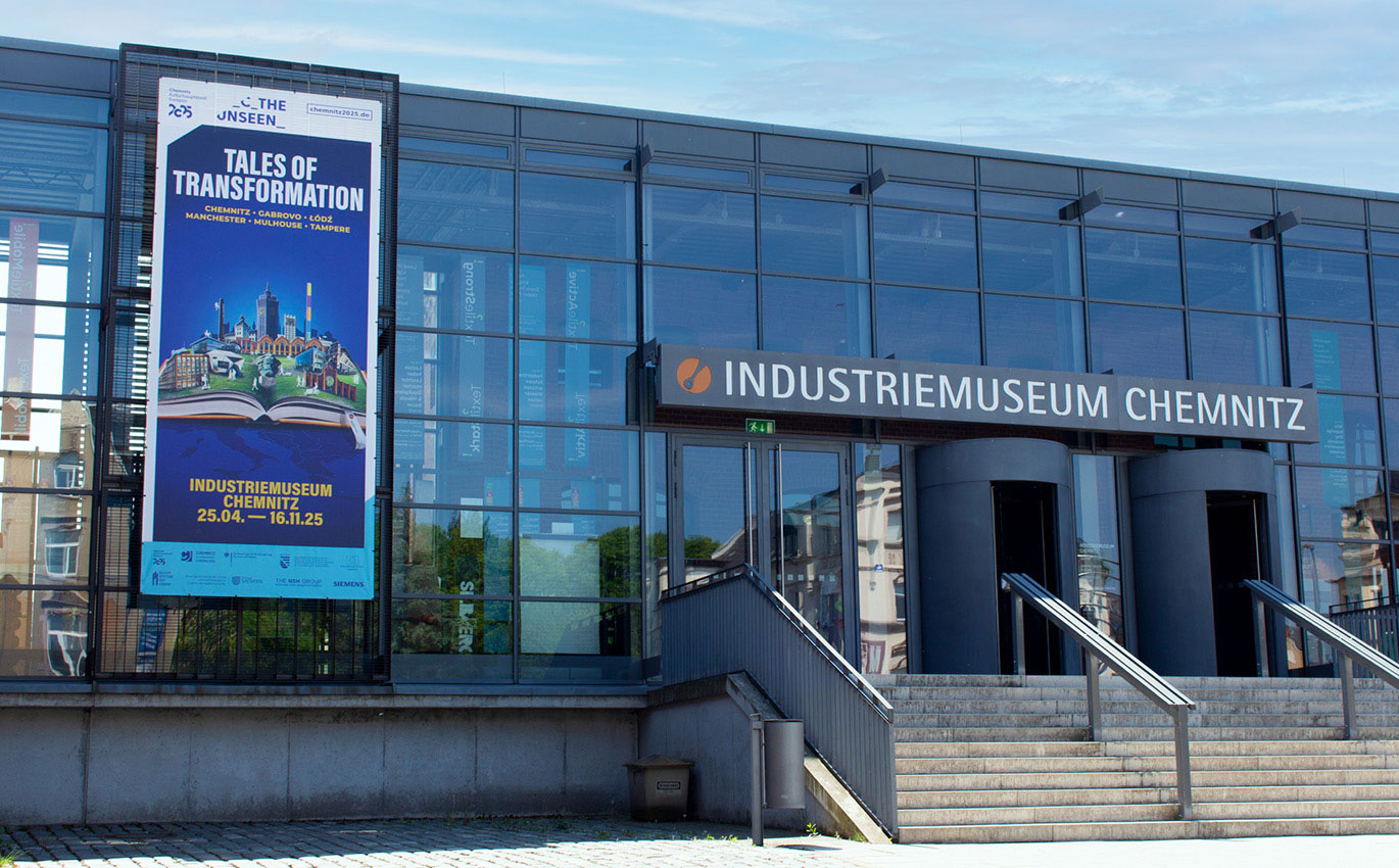 Mockup des Key-Visuals der Sonderausstellung Tales of Transformation. Ein aufgeschlagenes Buch ist vor einem blauen Hintergrund. Auf dem Buch sind einzelne Elemente der Stadt Chemnitz zu sehen, wie beispielsweise Gebäude oder Wahrzeichen.