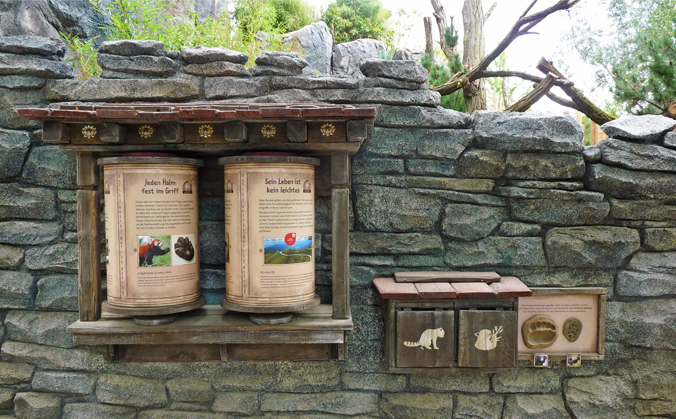 Scenographic learning station at Leipzig Zoo shows two Tibetan prayer wheels in combination of a discovery flap